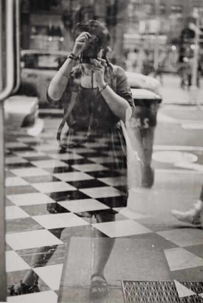 Grayscale image of a woman pointing a camera at her reflection.